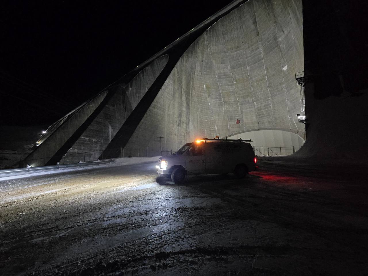 Fourgonnette de service avec gyrophare devant un grand barrage éclairé, de nuit