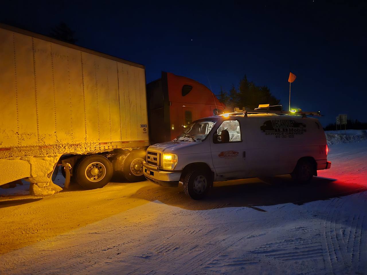 Fourgonnette de service avec gyrophare à côté d'un camion lourd et de sa remorque, de nuit dans la neige