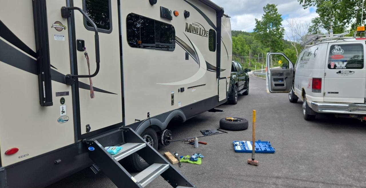 Roulotte en réparation sur le bord de la route, roue démontée et outils au sol
